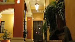 A corridor with a tiled floor, a large potted plant, and a door at the end. - Hotel de la Opera (Bogotá)