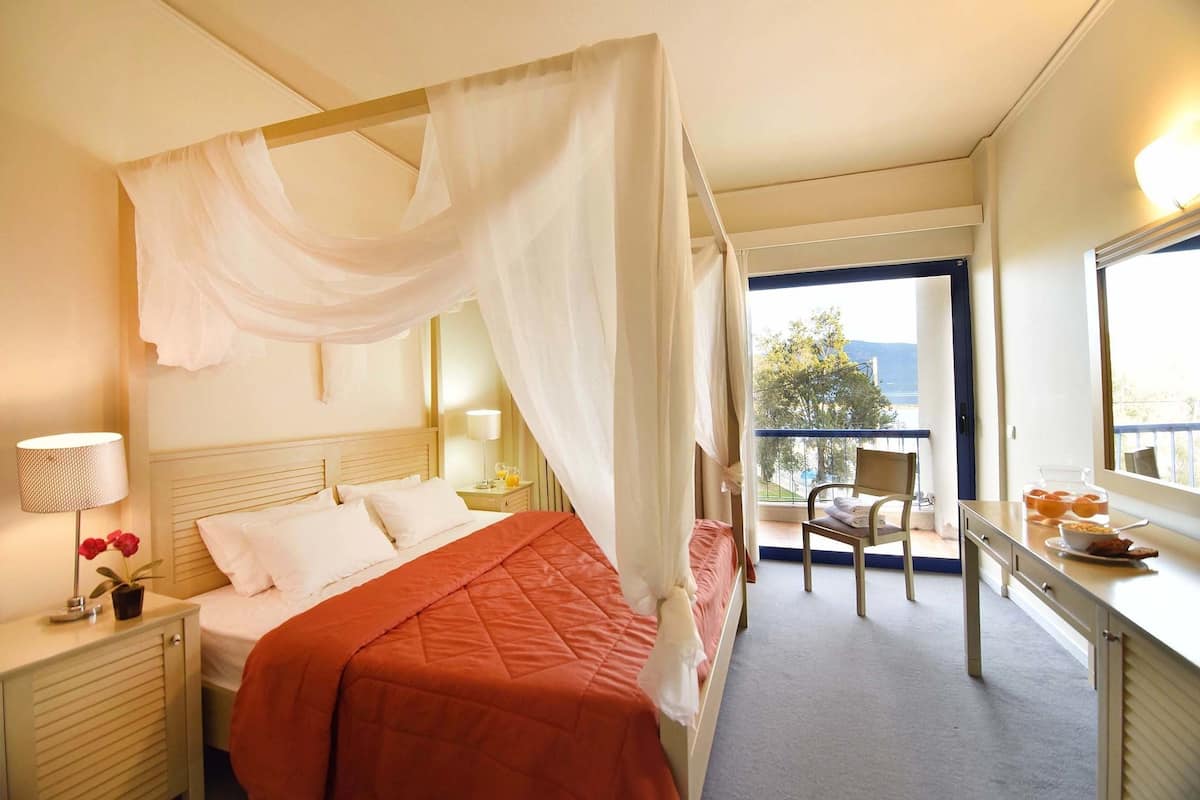 A hotel room with a four-poster bed, a balcony with a chair, and a view of the outdoors.