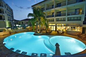 A swimming pool with lounge chairs and a bar area, surrounded by multi-story buildings with balconies. - Ionion Star Hotel (Lefkada)