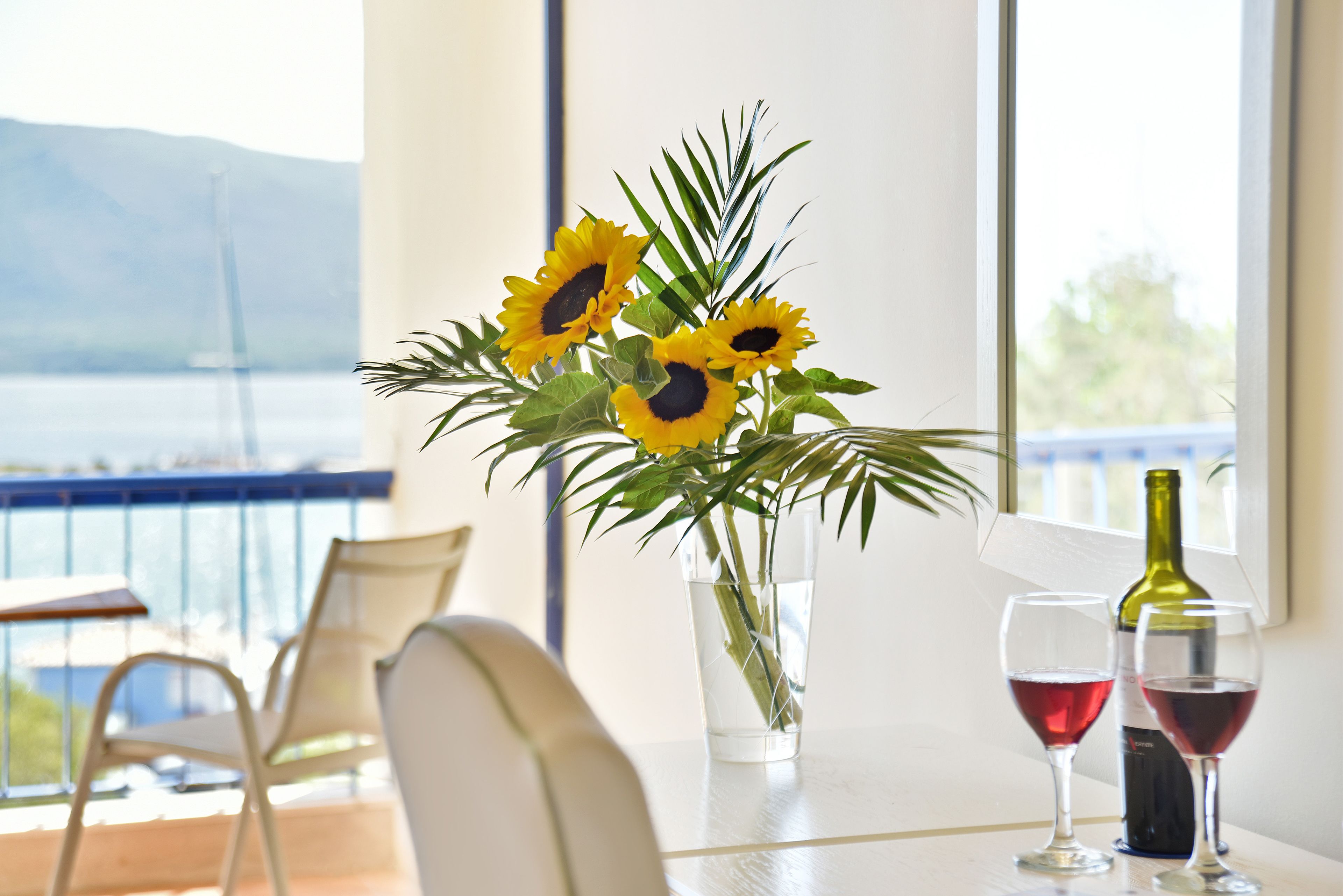 A table with a vase of sunflowers, two wine glasses, and a wine bottle.