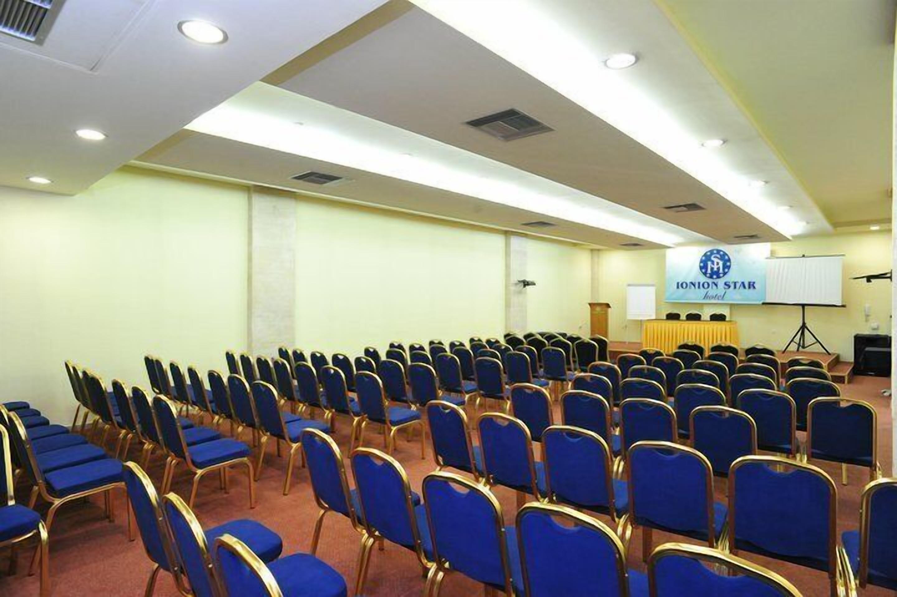 A conference room with rows of blue chairs and a podium with a screen.