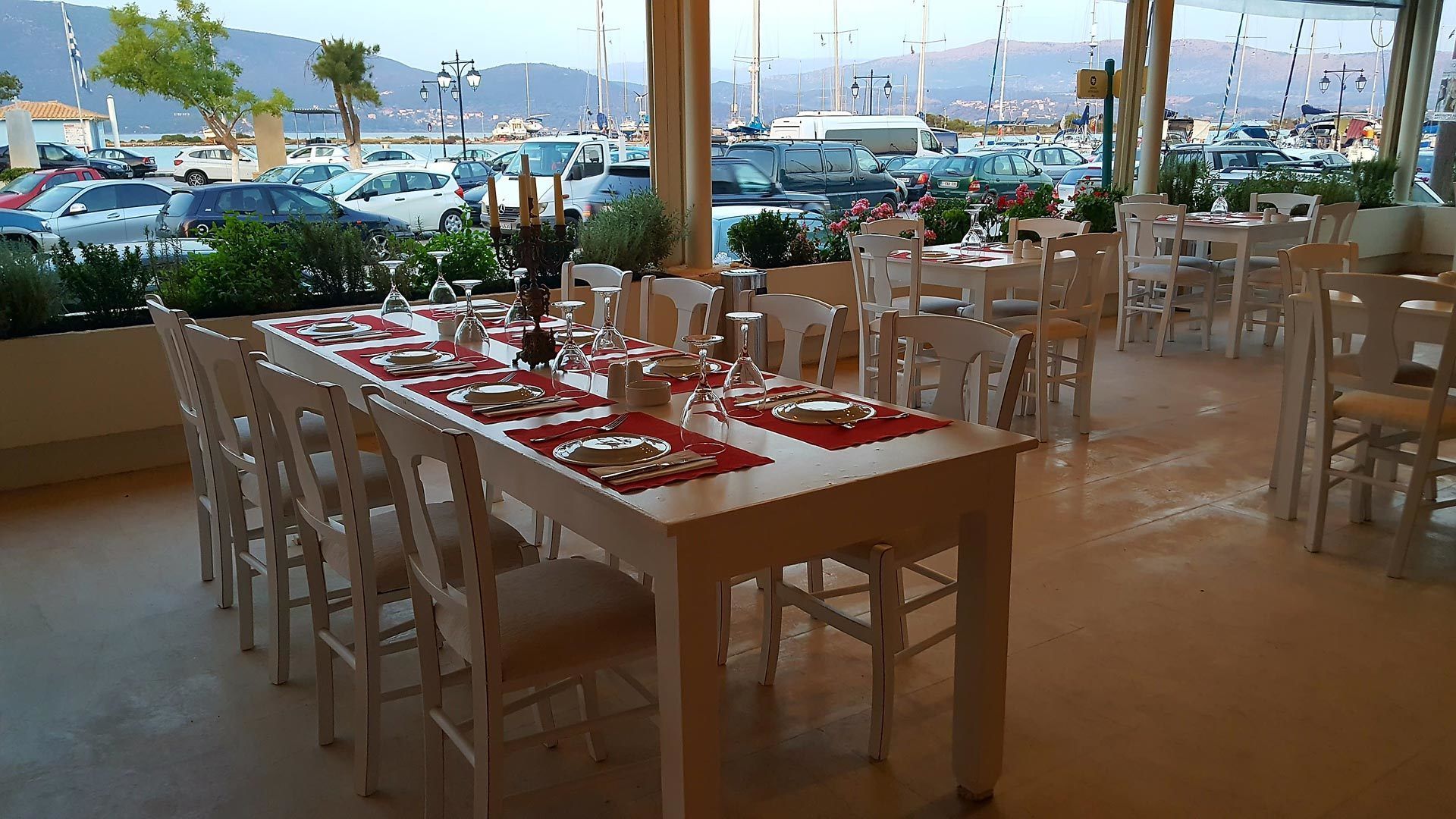 A dining area with tables set for a meal, overlooking a marina with boats.