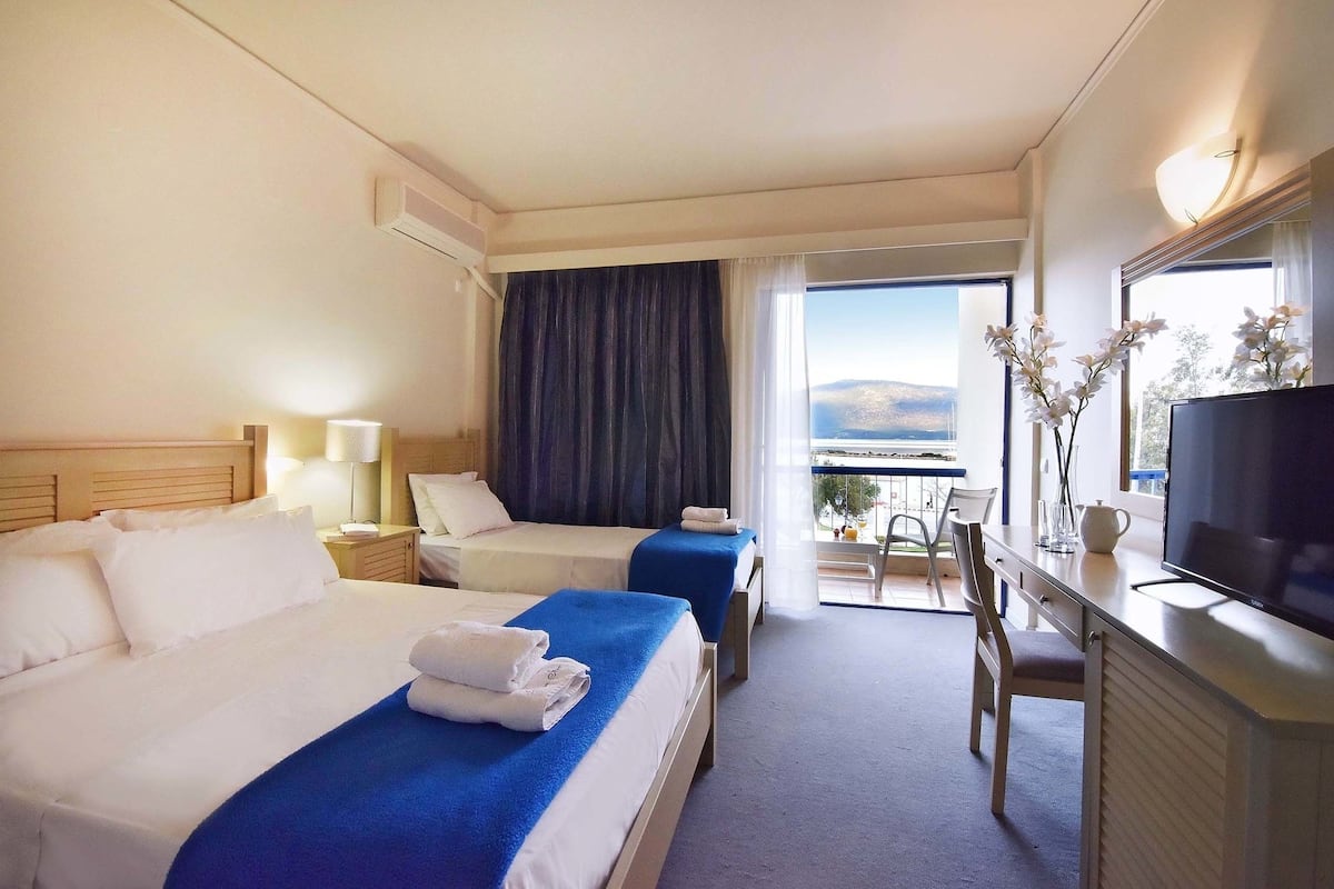A hotel room with two beds, a desk with a TV, and a balcony with a view.