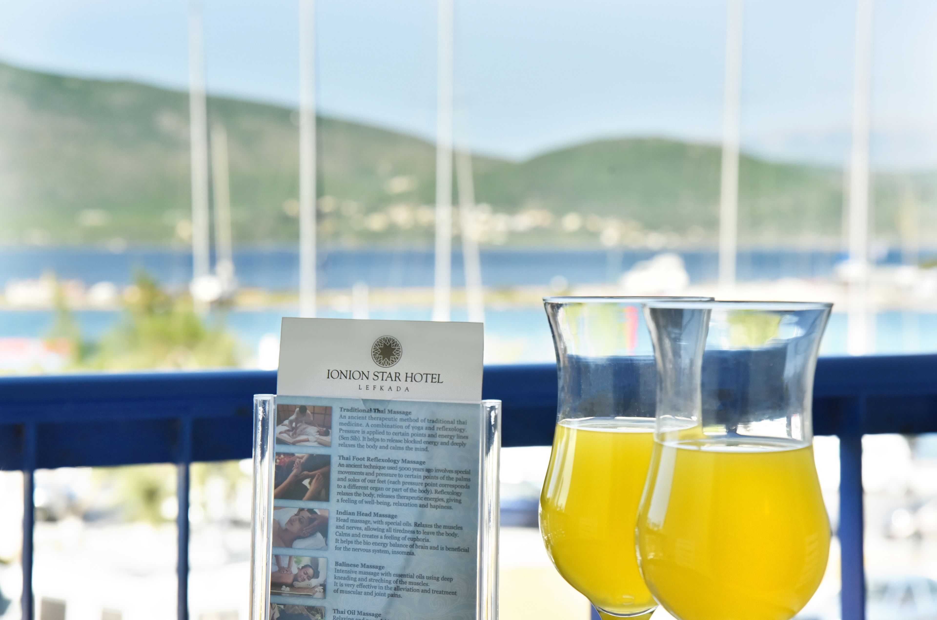 Une enseigne indiquant l’hôtel Ionion Star à Lefkada, avec une description des services de massage proposés, et deux verres d’une boisson jaune en premier plan.