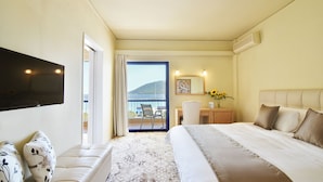 Habitación de hotel con una cama grande, un televisor de pantalla plana en la pared, un escritorio con silla y un balcón con vistas al mar.