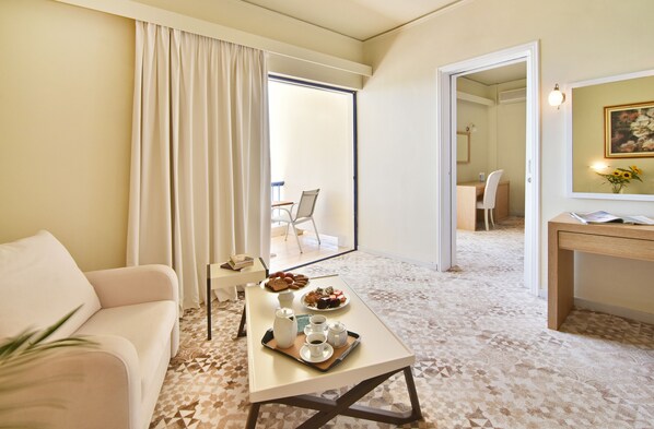 A hotel room with a sofa, a dining table with a tray of food, a coffee station, and a large mirror reflecting the room. - Ionion Star Hotel (Lefkada)