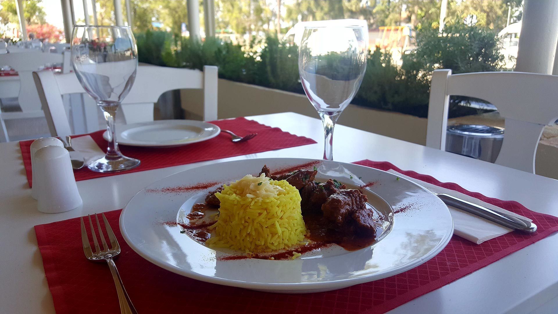 A dining table with a plate of yellow rice and meat, a fork, and a wine glass.