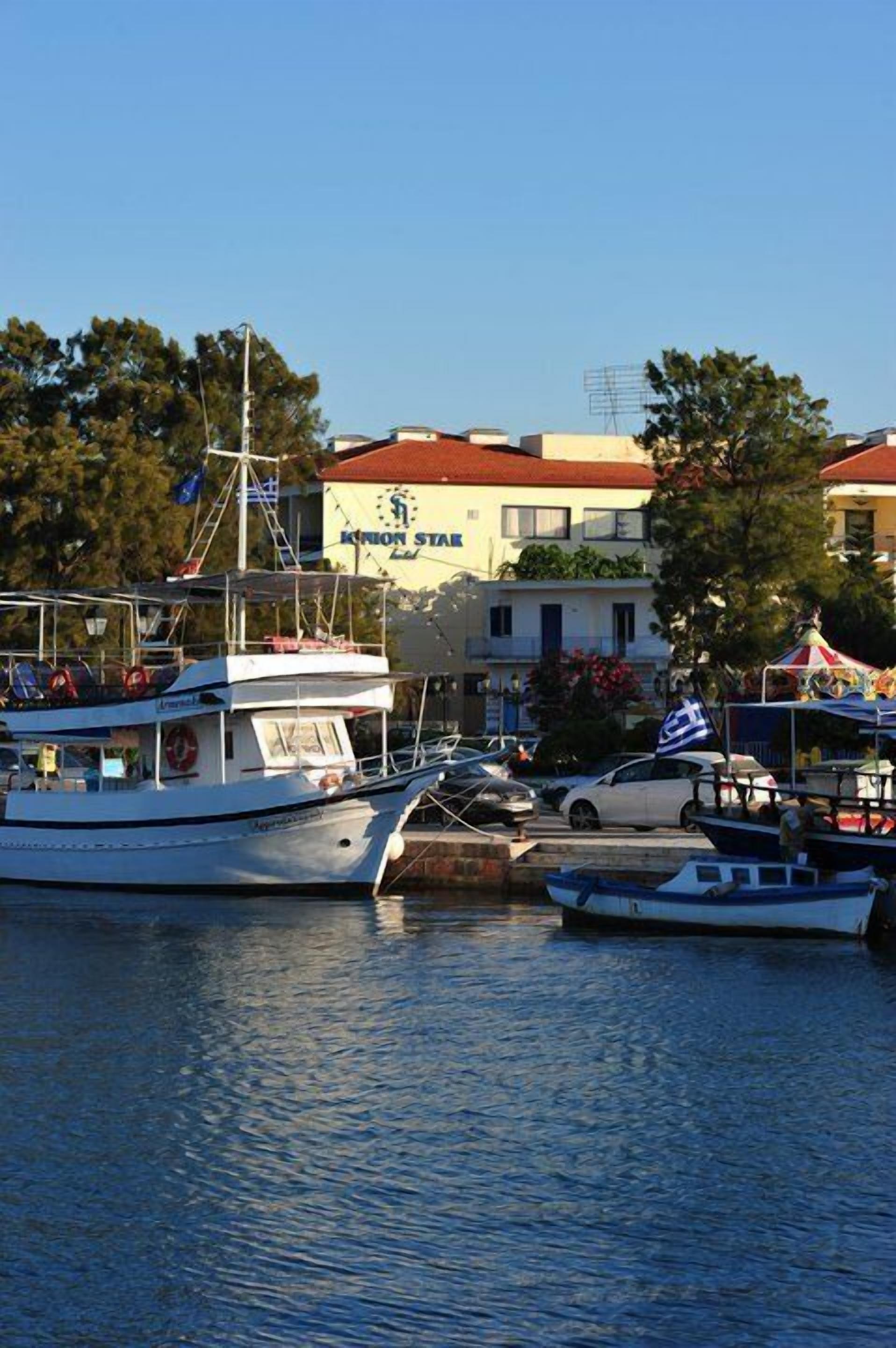 A marina with boats docked, a building with a sign reading "KARION STAR," and a flag on a nearby structure.