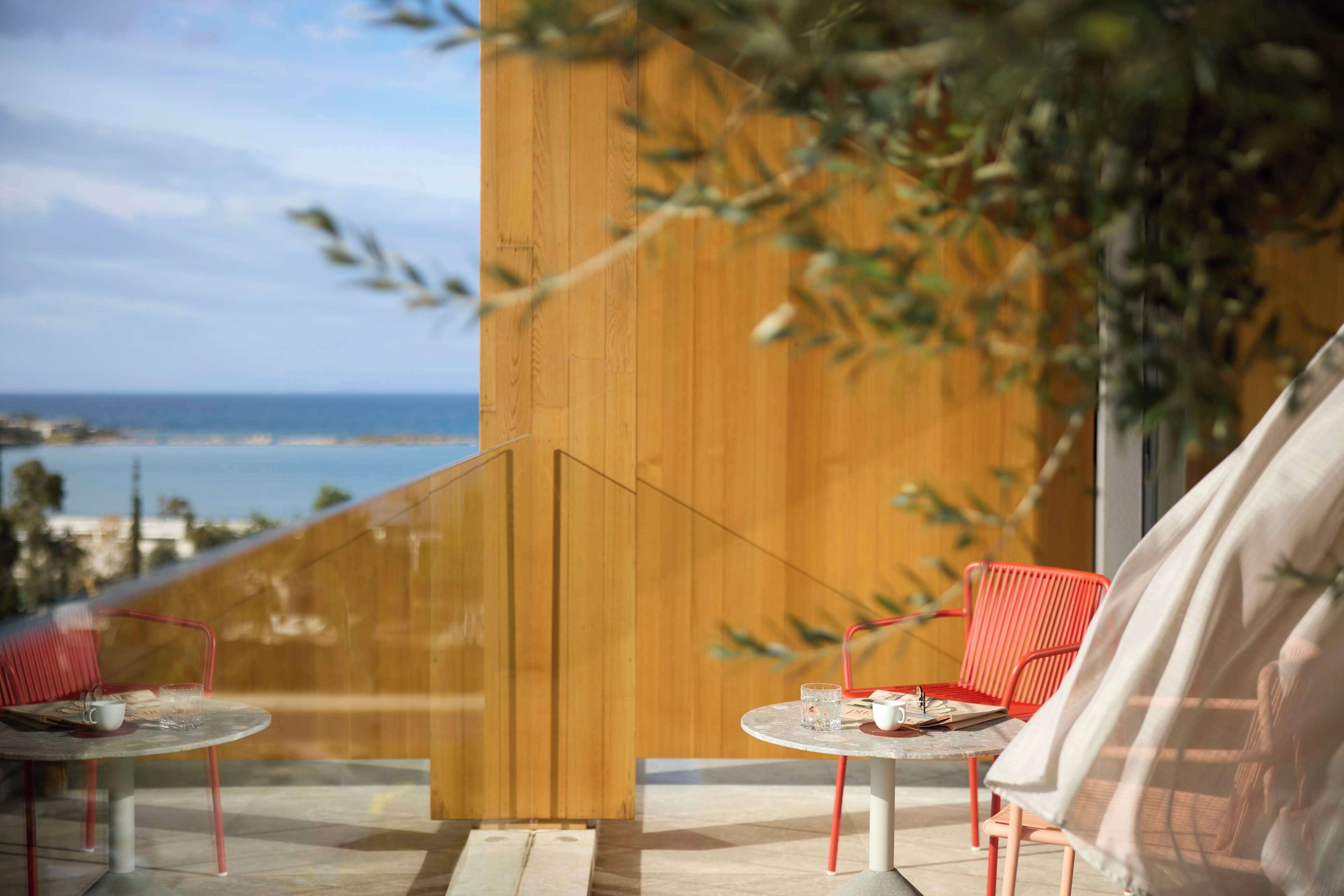 Un balcone con due sedie rosse e un tavolo, affacciato su una vista costiera.