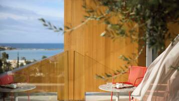 Un balcone con due sedie rosse e un tavolo, affacciato su una vista costiera.