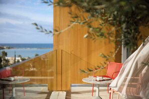 A balcony with two red chairs and a table, overlooking a coastal view. - Dusit Suites Athens (Glyfada)