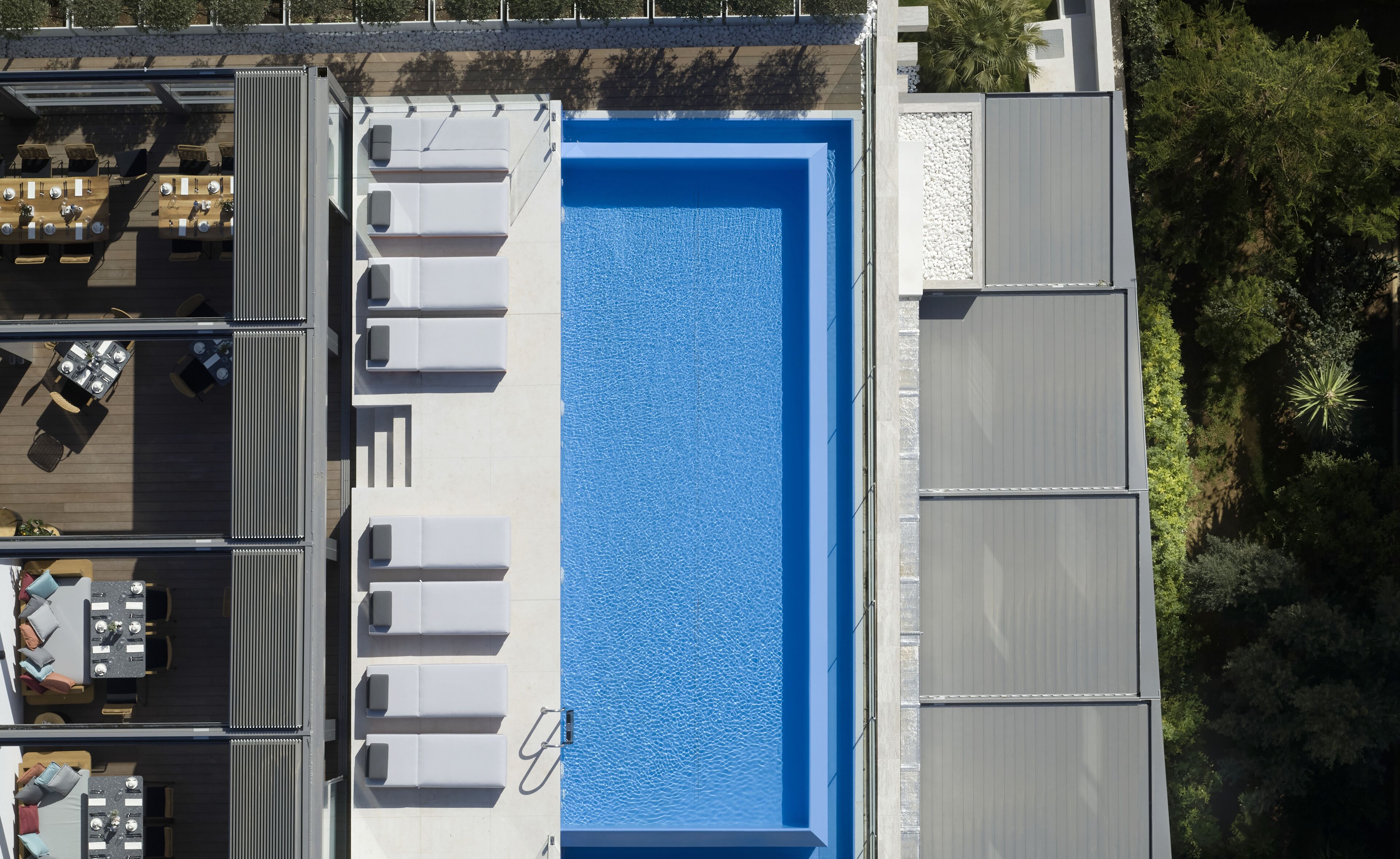 A rooftop pool with a blue interior, surrounded by lounge chairs and tables.