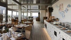 A modern restaurant with high ceilings, large windows, and a view of the city. - Dusit Suites Athens (Glyfada)