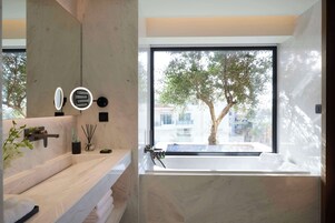 Uma casa de banho moderna com um espelho grande, uma pia e uma banheira. Há uma janela com vista para árvores e edifícios.