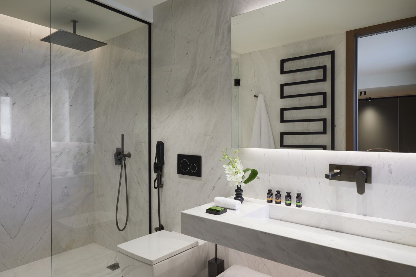 A modern bathroom with a glass-enclosed shower, a white sink with a marble countertop, and a large mirror.