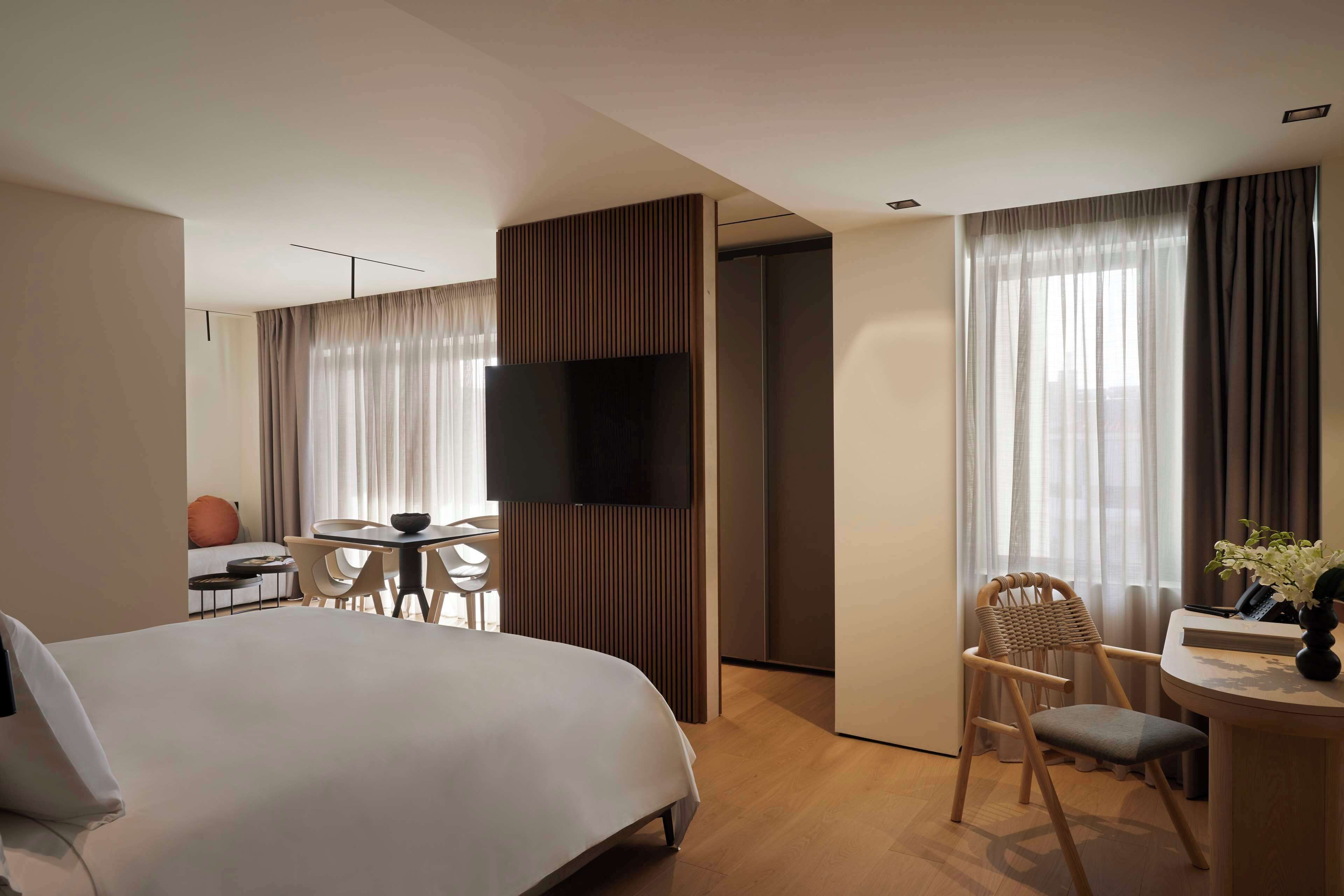 A hotel room with a large bed, a desk with a chair, a television, and a window with curtains.