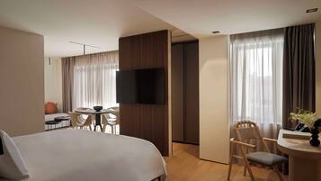 A hotel room with a large bed, a desk with a chair, a television, and a window with curtains.