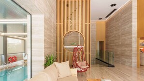 A modern interior with a pool, a red hanging chair, and a wooden partition. - Dusit Suites Athens (Glyfada)