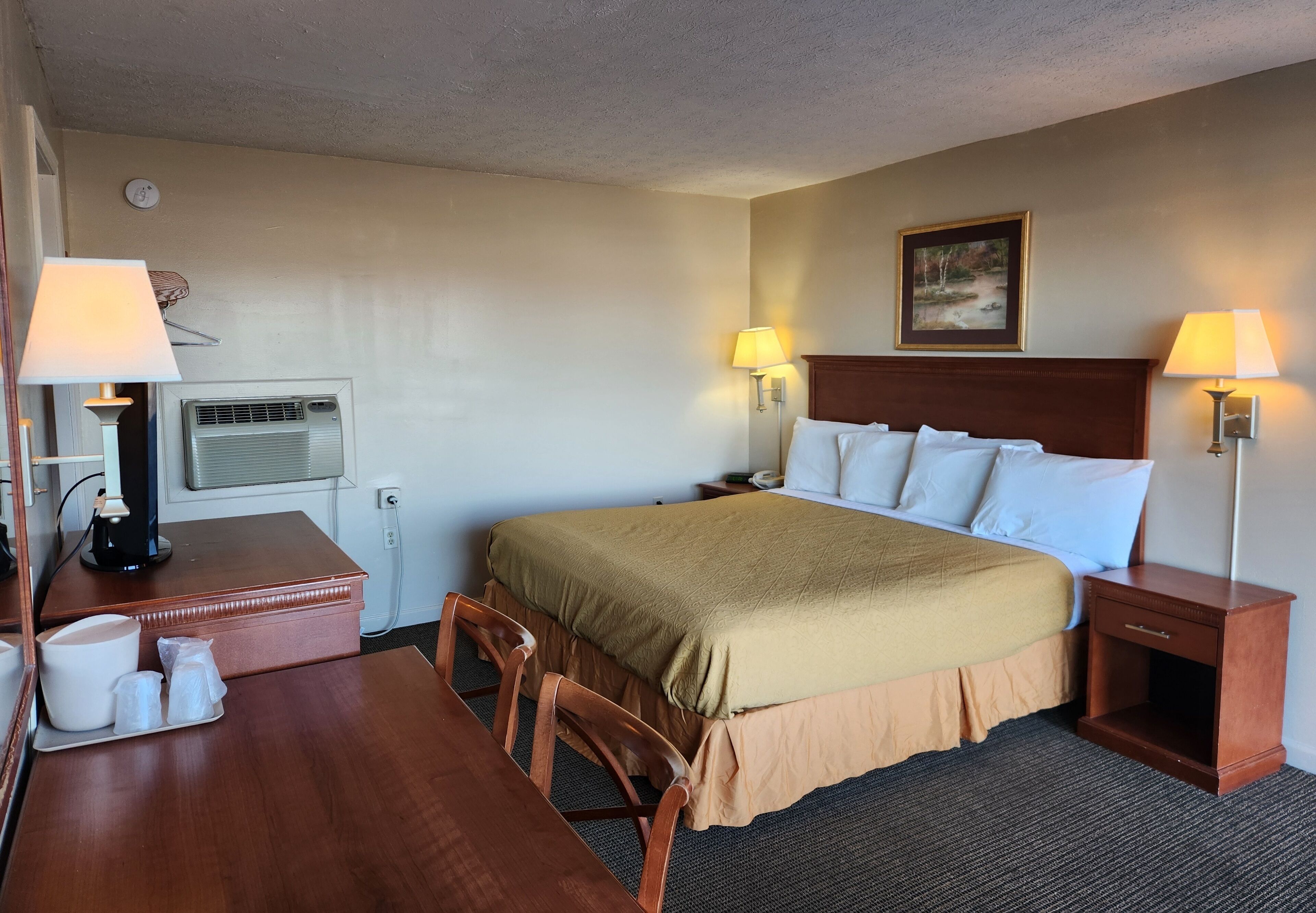 Une chambre d’hôtel avec un lit, des lampes de chevet, un bureau avec une lampe, une machine à café et un tableau au mur.