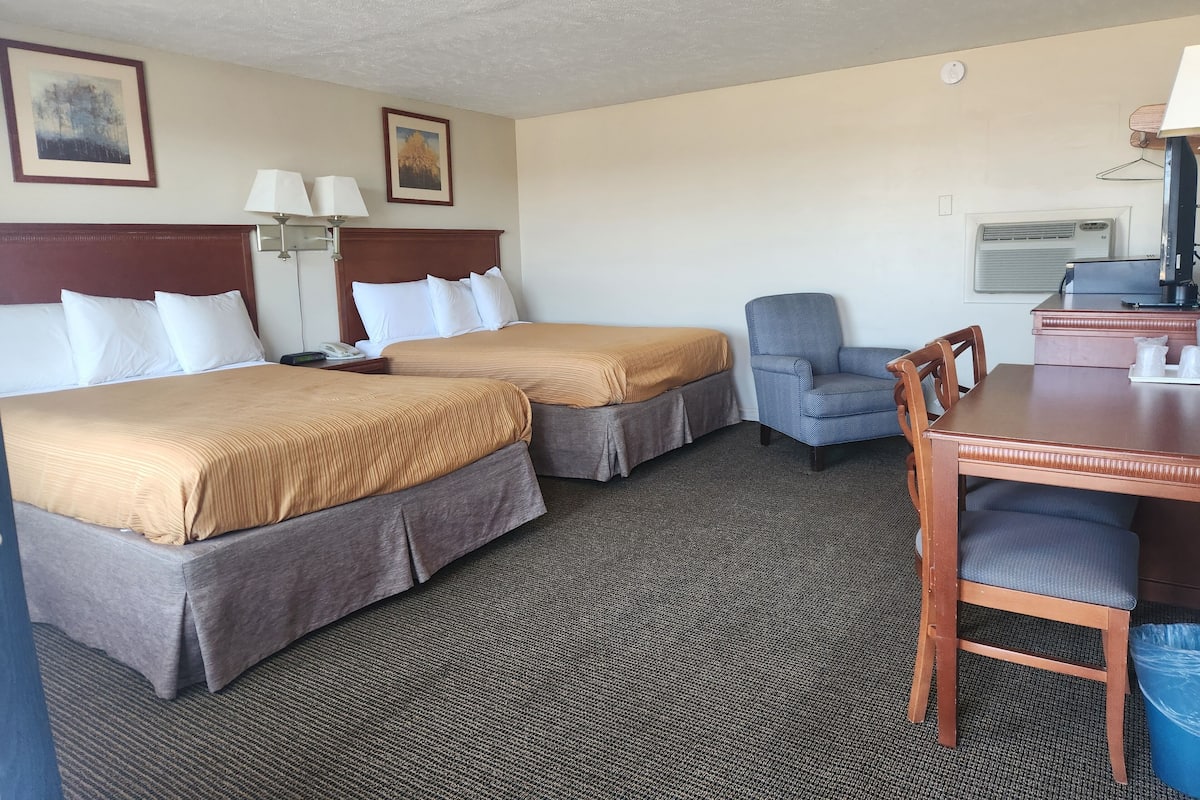 A hotel room with two beds, a desk, a chair, a lamp, and a picture on the wall.
