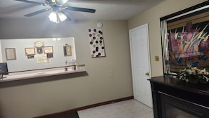 A hallway with a ceiling fan, a bulletin board with various notices, a door, and a fireplace with a decorative mirror. - Royal Motel (Hermitage)