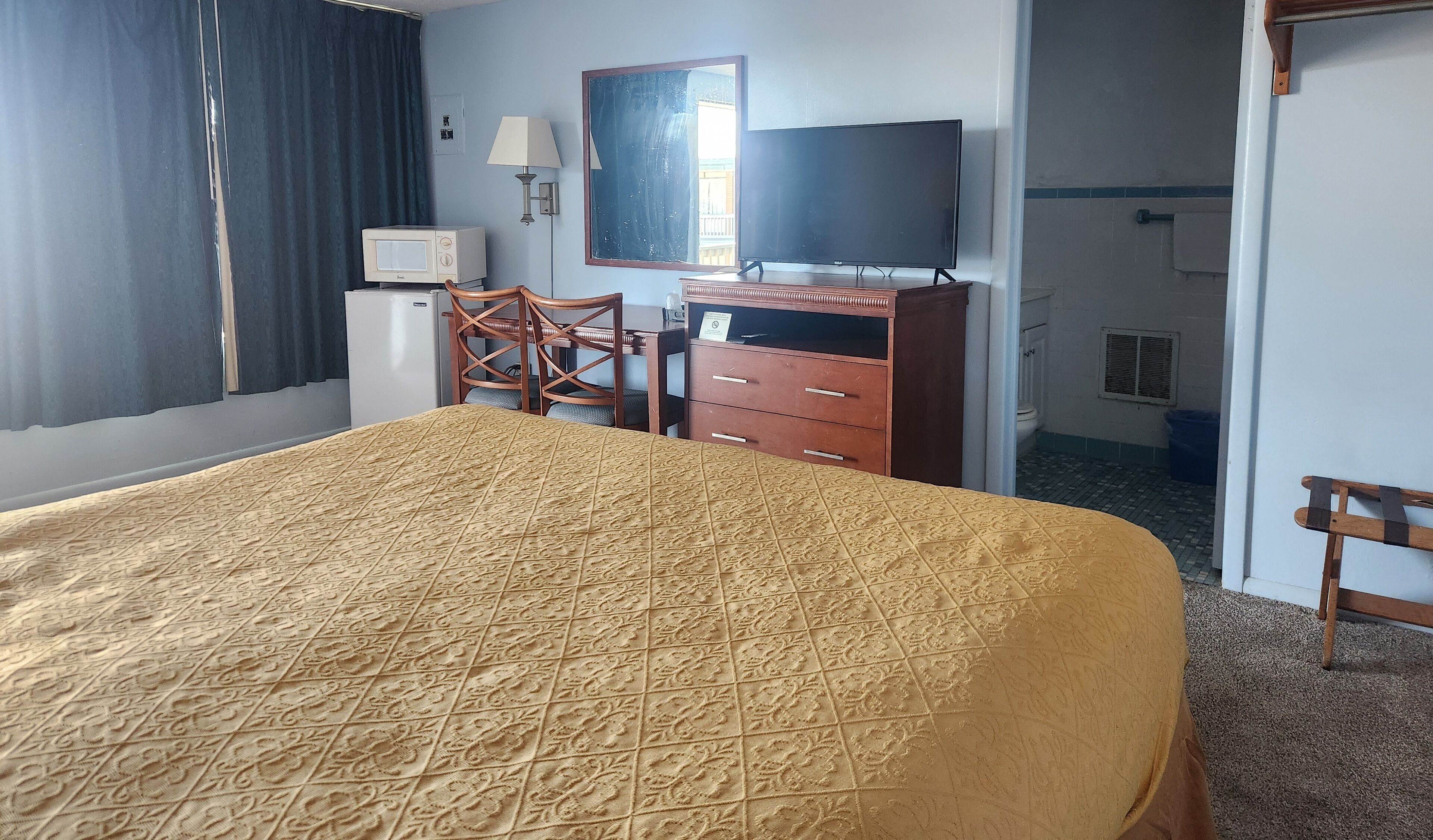 A hotel room with a bed, a desk, a chair, a television, a dresser, and a window with curtains.