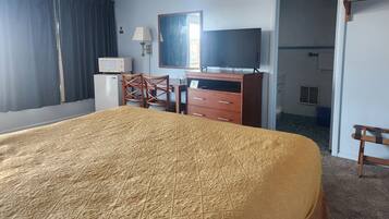A hotel room with a bed, a desk, a chair, a television, a dresser, and a window with curtains.