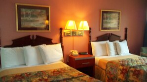 A hotel room with two beds, each with a floral bedspread, a wooden headboard, and a nightstand with a lamp. There are two framed pictures on the wall. - Royal Motel (Hermitage)