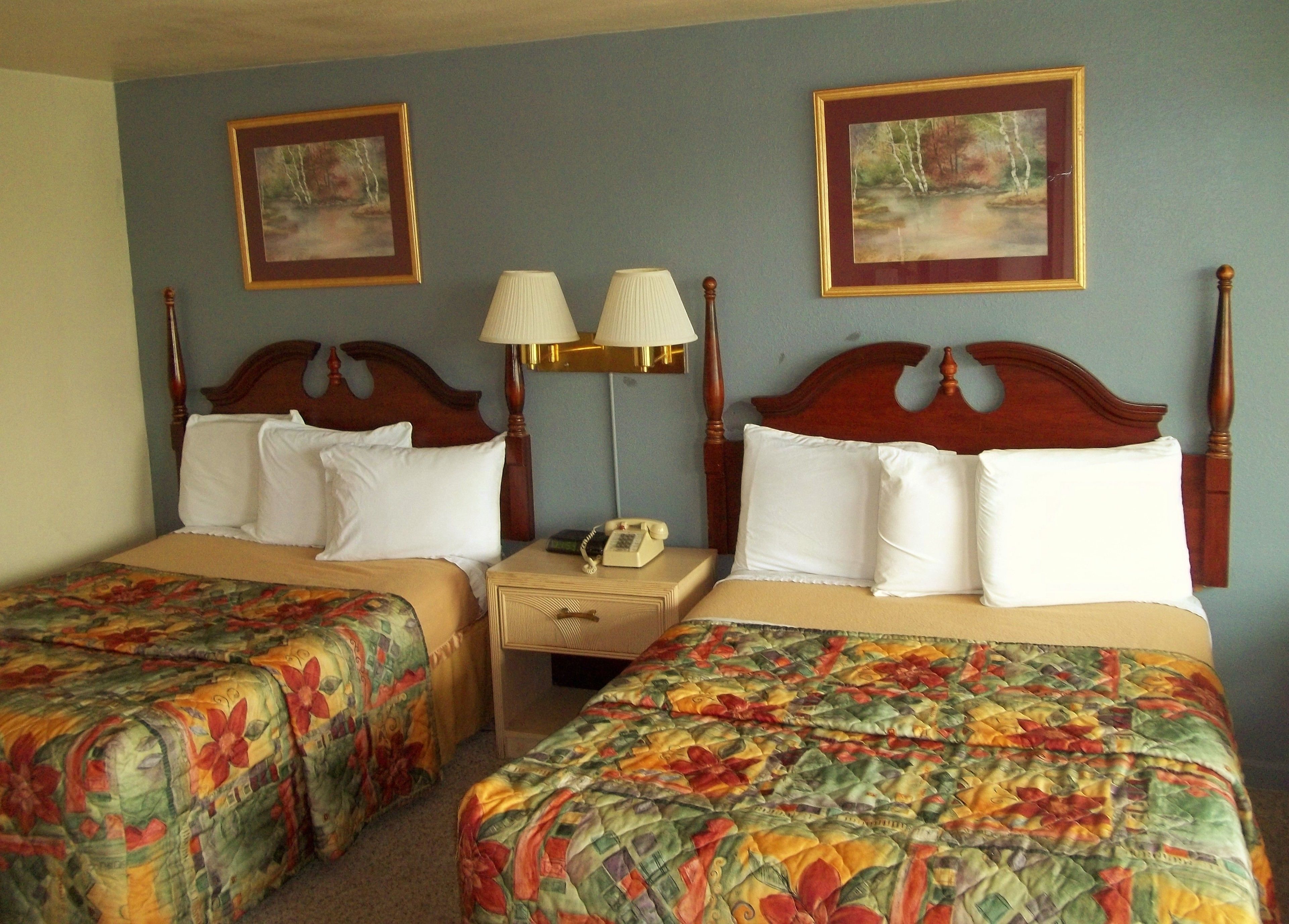A hotel room with two beds, each with floral bedspreads, a nightstand with lamps, and framed artwork on the walls.
