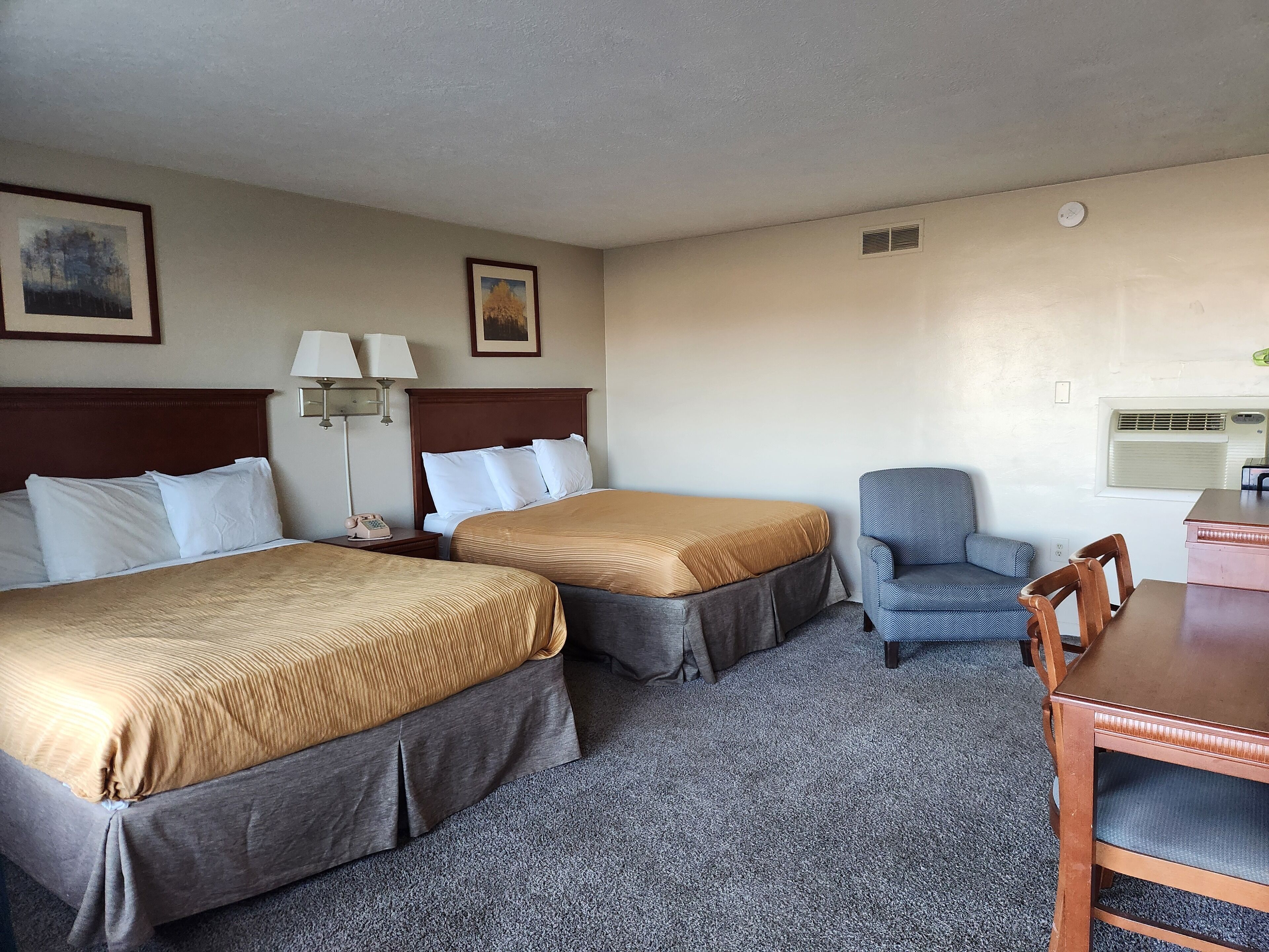A hotel room with two beds, a desk, a chair, and a lamp.