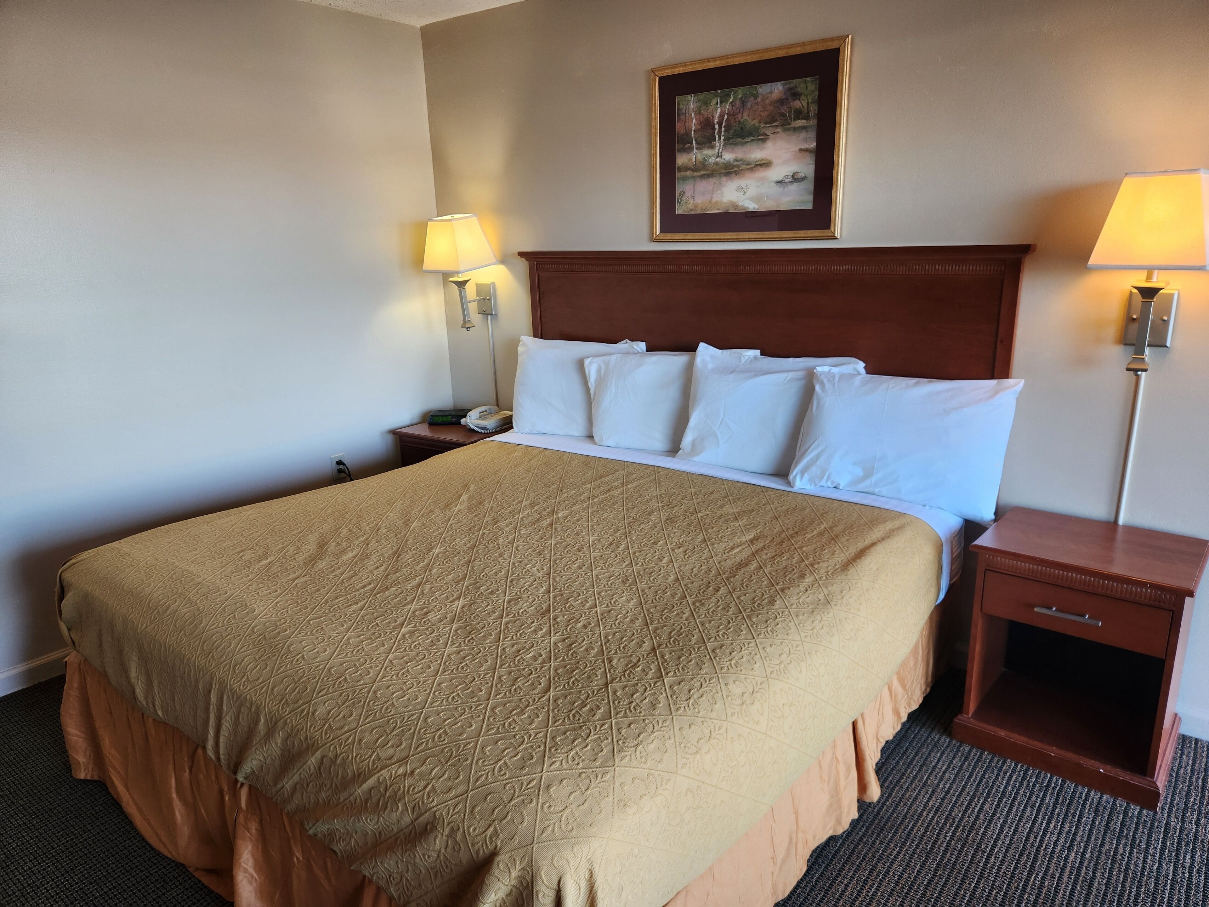 A hotel room with a large bed, two bedside tables, a nightstand, a headboard, and a framed picture on the wall.