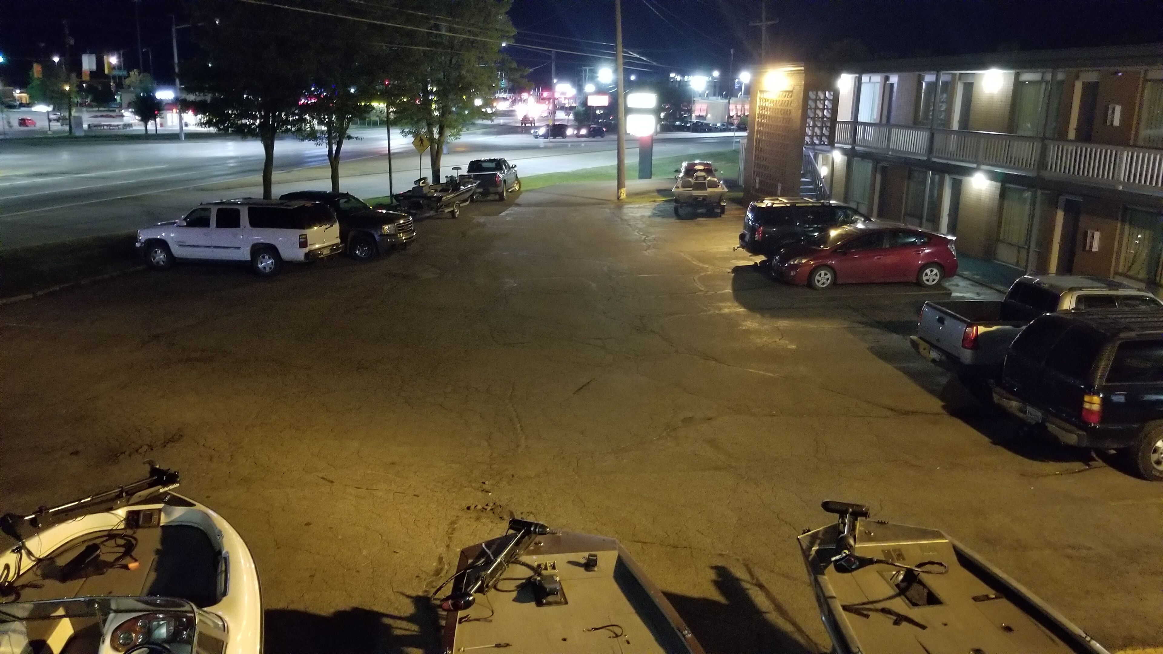 Un estacionamiento con varios vehículos, incluyendo camiones y automóviles, aparcados cerca de un edificio con balcón.
