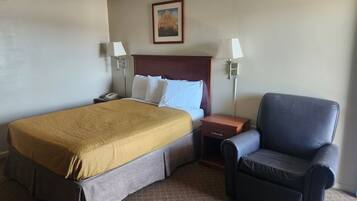 Habitación de hotel con una cama grande, dos mesitas de noche, una silla, un cuadro en la pared y suelo alfombrado.