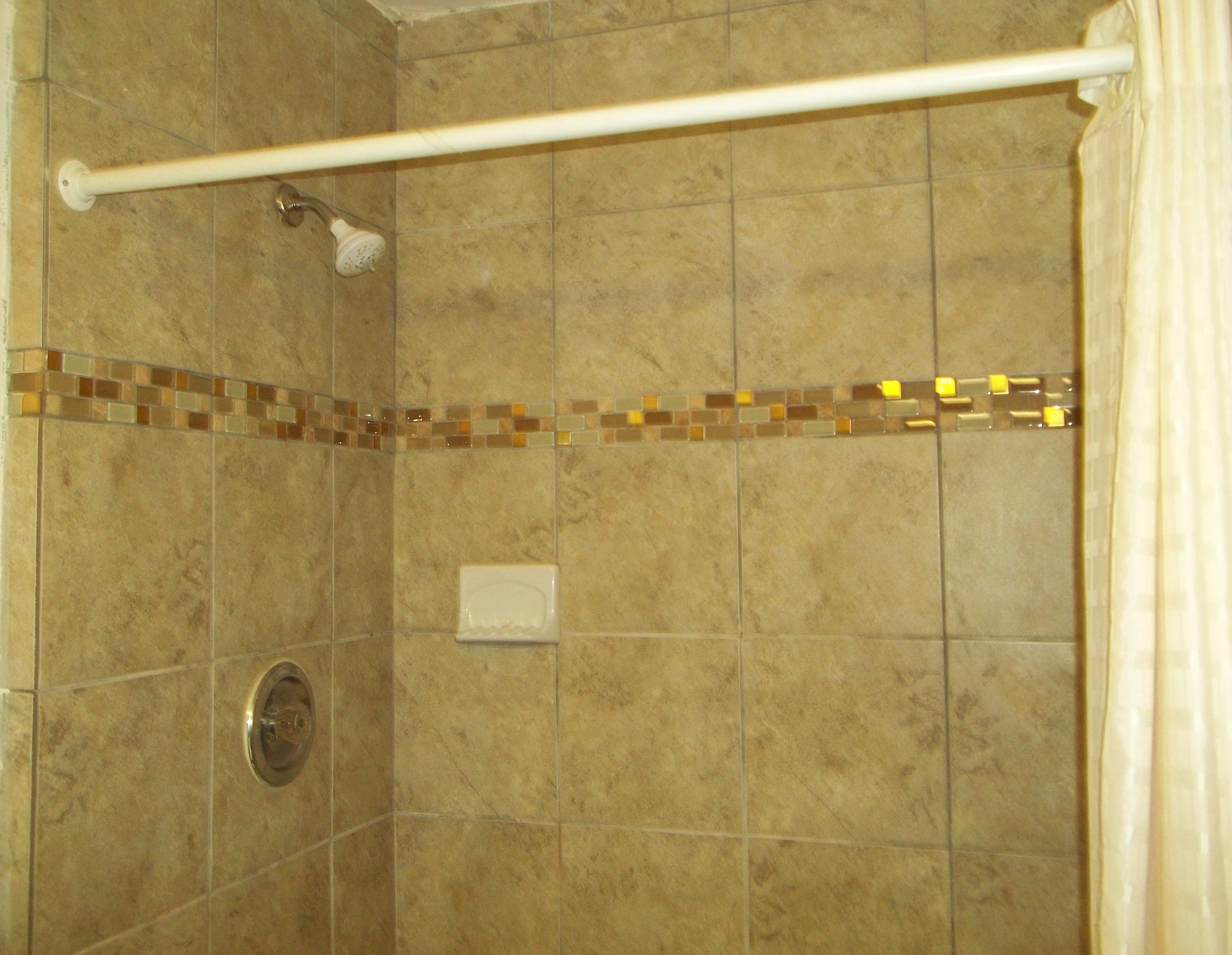 A shower with beige tiles, a white towel bar, and a showerhead.