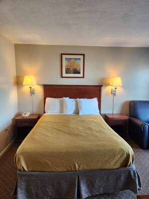 A hotel room with a large bed, two bedside lamps, a telephone, a framed picture on the wall, and a chair. - Royal Motel (Hermitage)