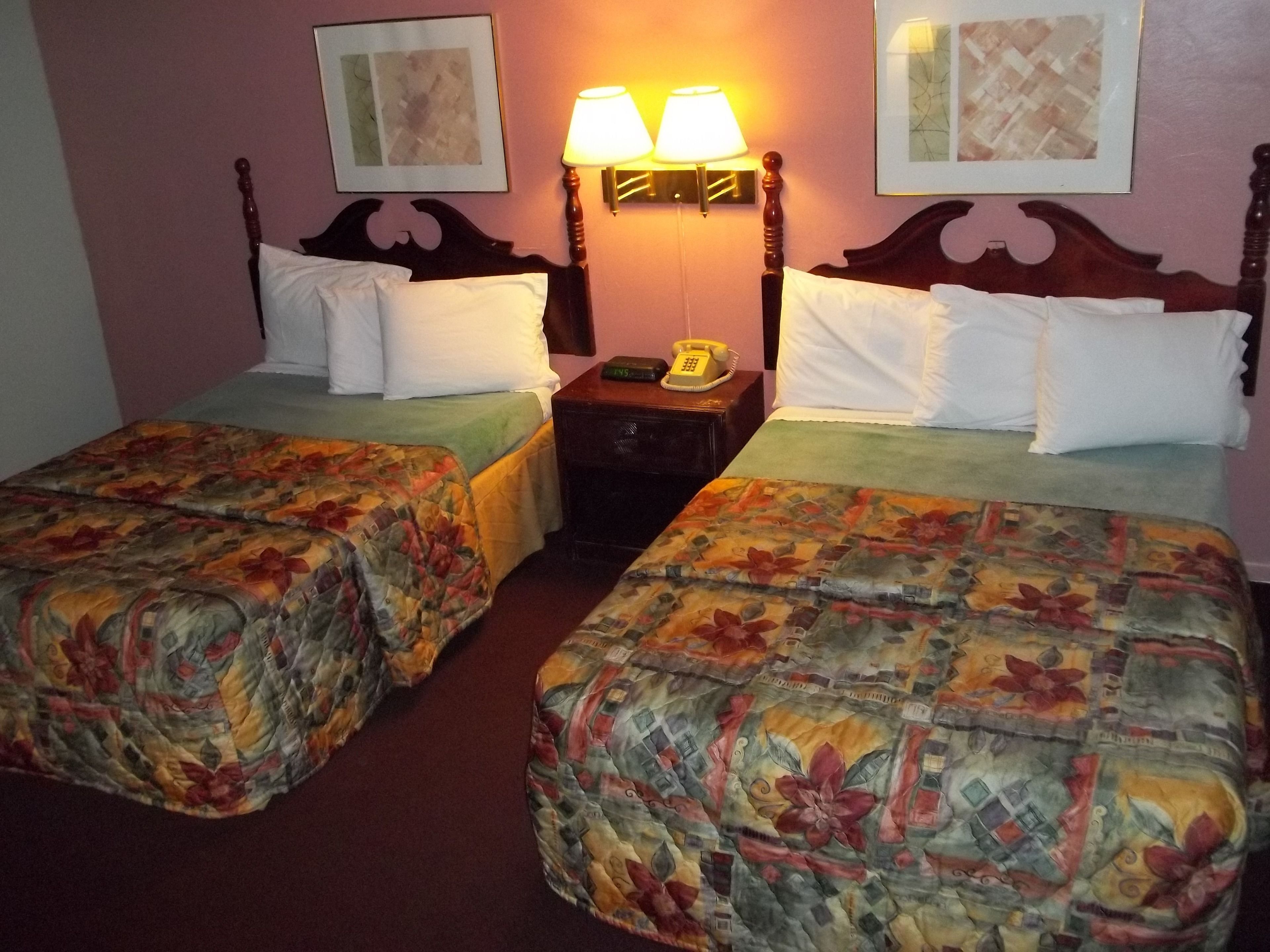 Una habitación de hotel con dos camas, cada una con ropa de cama floral, una mesita de noche con teléfono y lámparas de pared.