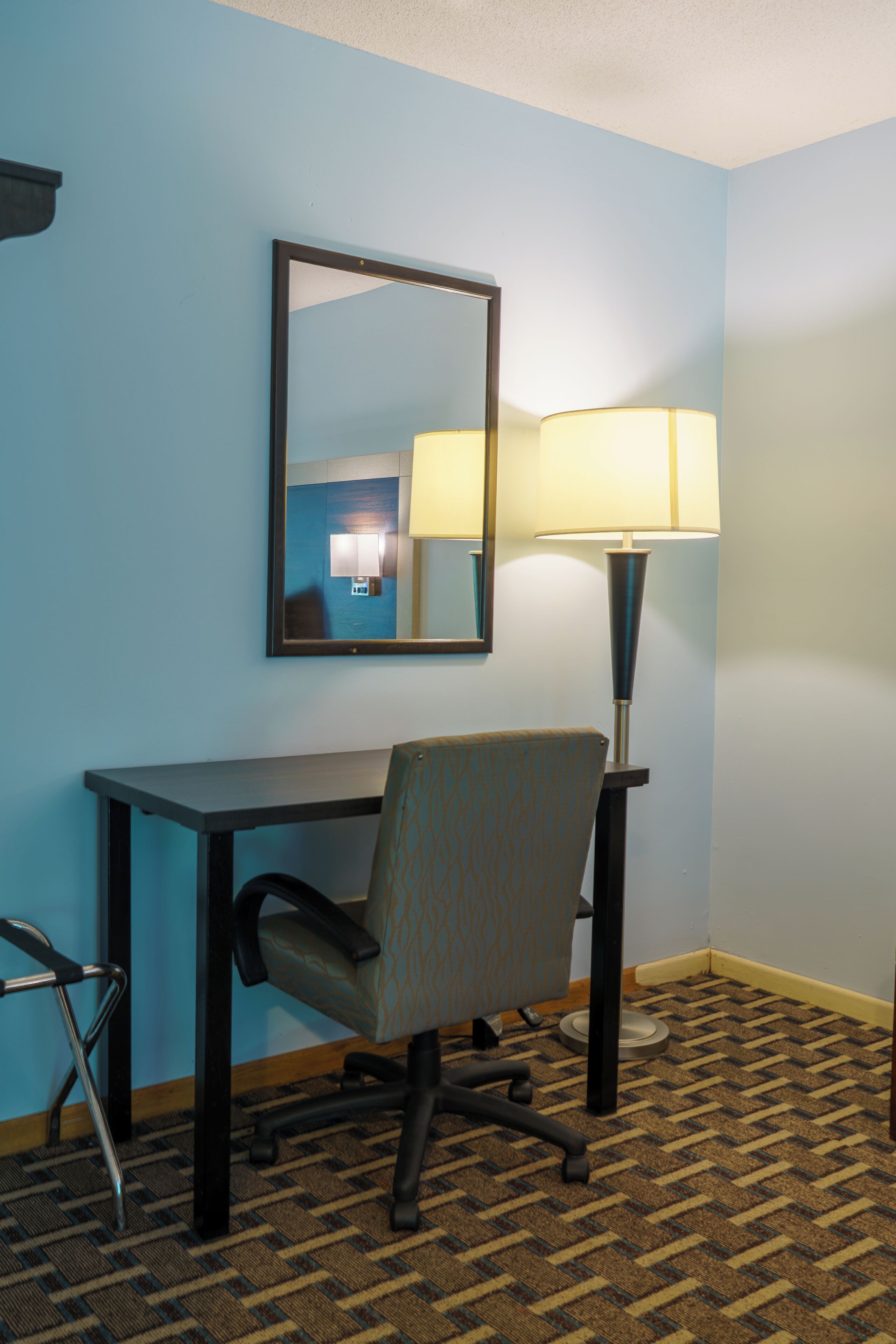 Una habitación de hotel con escritorio, silla, lámpara y espejo en la pared.