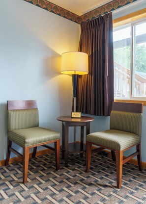 Een hoekappartement met twee gestoffeerde fauteuils, een tafel met een lamp en een raam met gordijnen.