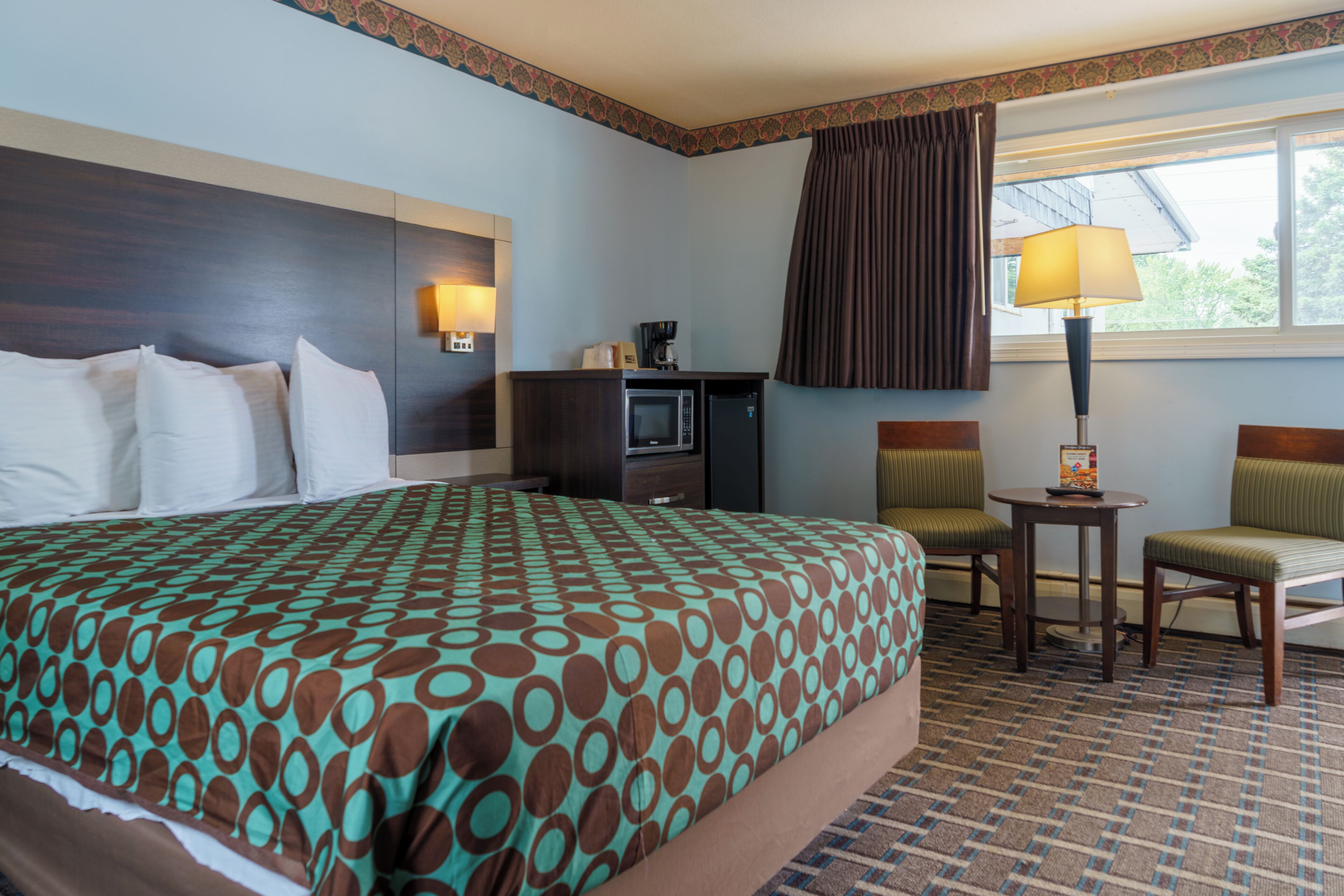Une chambre d’hôtel avec un grand lit, un bureau, une chaise, une lampe et une fenêtre avec des rideaux.