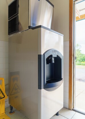 A commercial kitchen with stainless steel appliances, a push ice dispenser, and a caution sign on the floor. - Budget Host Inn Fridley (Fridley)