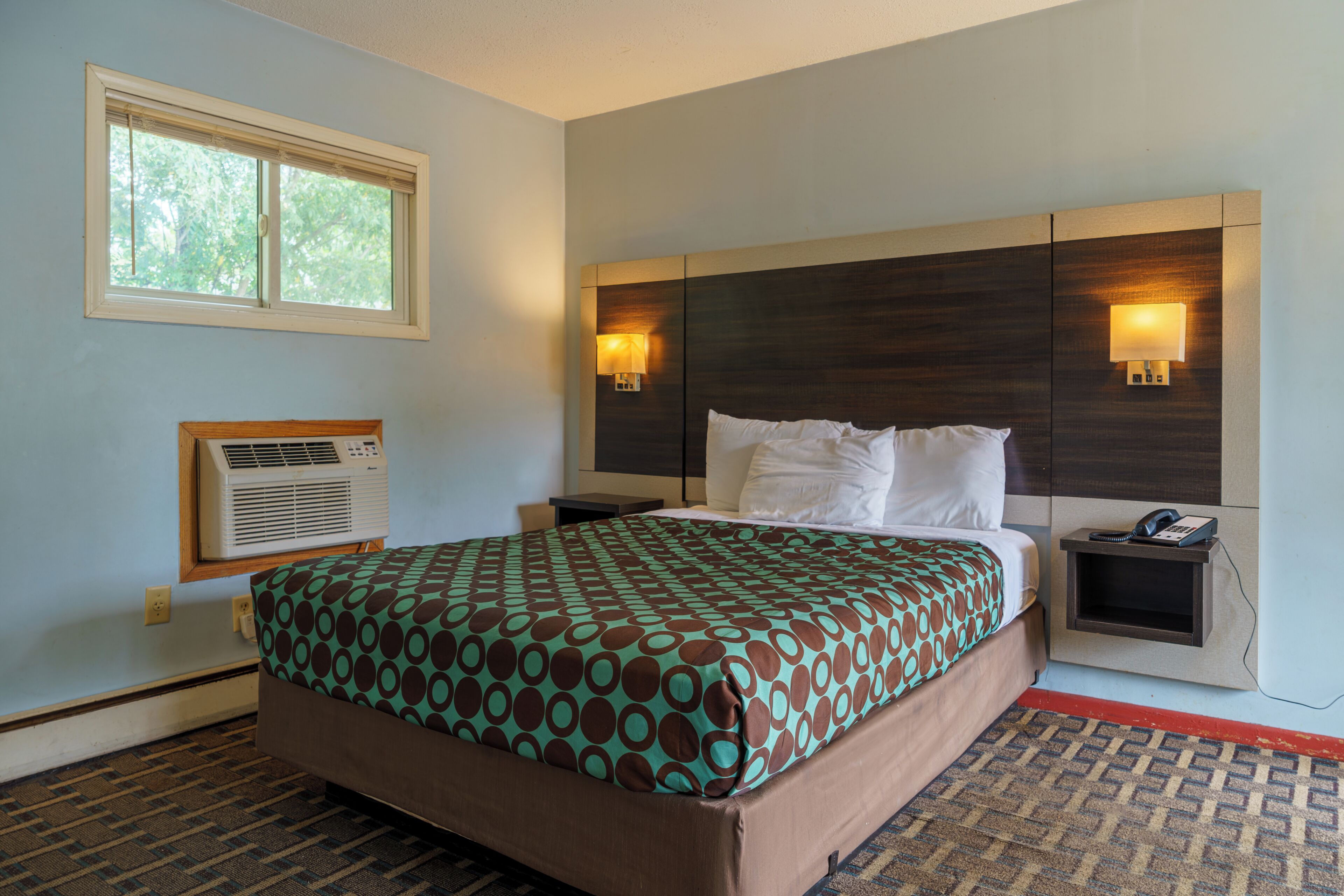 A hotel room with a bed, bedside tables, a phone, and a window.