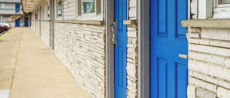 A row of blue doors with a stone facade, a covered walkway, and a clear sky.
