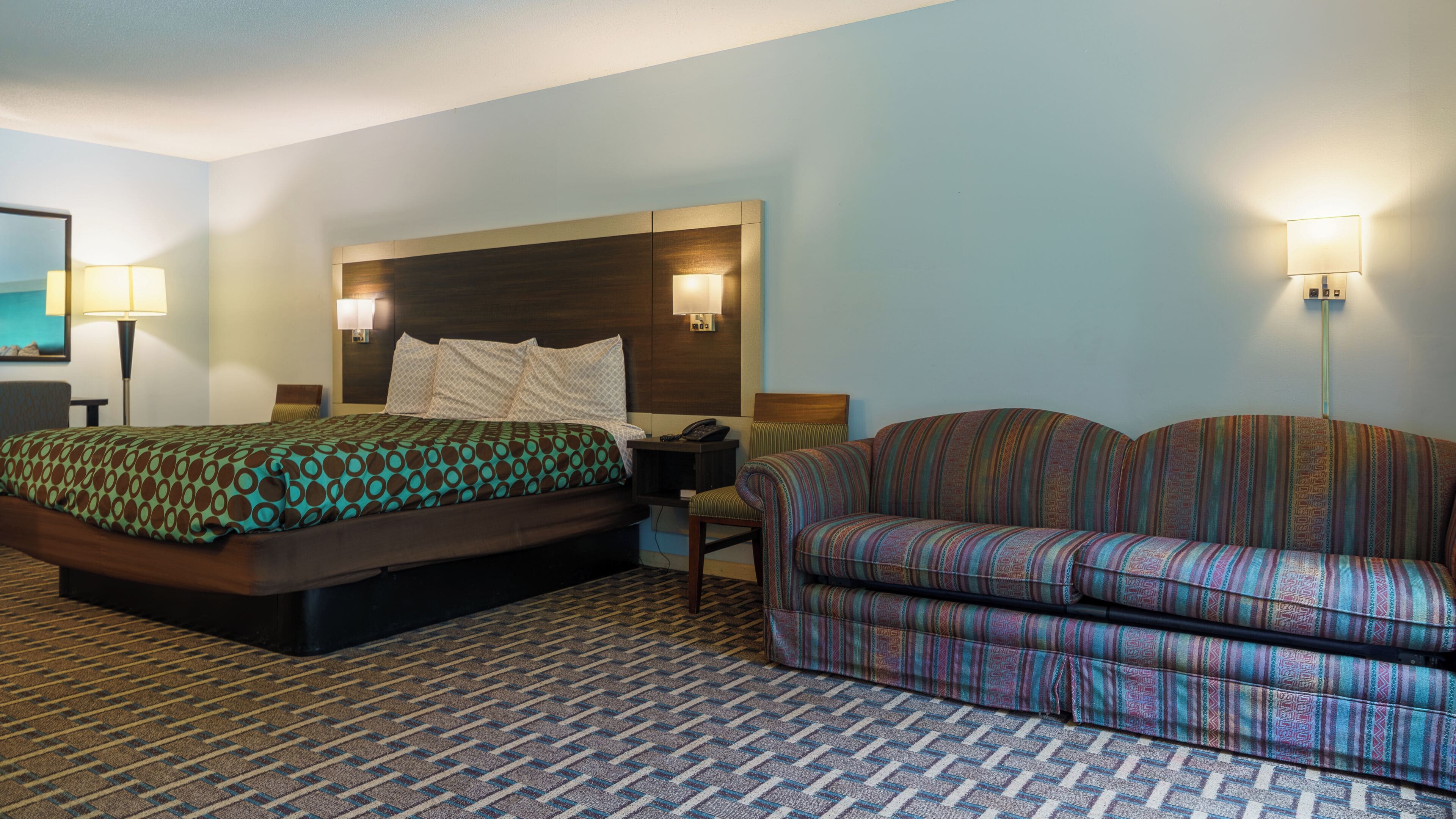 A hotel room with two beds, a sofa, a lamp, and a wall-mounted phone.