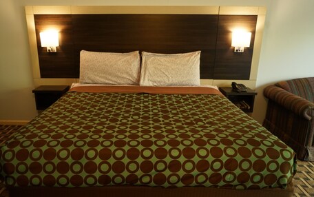 A hotel room with a large bed, two bedside tables, a chair, and a headboard with wall-mounted lights.