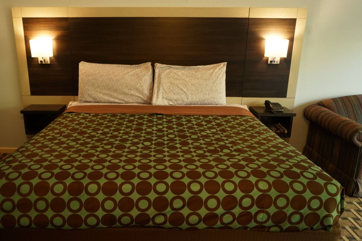 A hotel room with a large bed, two bedside tables, a chair, and a headboard with wall-mounted lights.