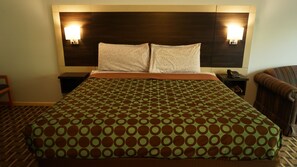 A hotel room with a large bed, two bedside tables, a chair, and a headboard with wall-mounted lights.