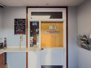 A reception desk with a sign indicating a 20-minute wait for attendants, a no pets policy with a $100 fine, and a guest guide stand. - Budget Host Inn Fridley (Fridley)