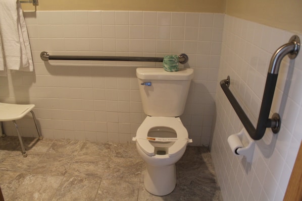 A bathroom with a white toilet, a grab bar, a towel rack, and a white sink.