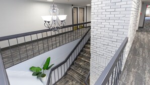 A multi-level interior with a staircase, a hanging light fixture, and a potted plant. - Coratel Inn & Suites by Jasper Mankato (Mankato)