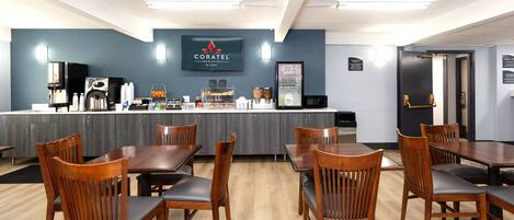 A restaurant with wooden tables and chairs, a counter with a coffee machine, and a sign reading "CORATEL".